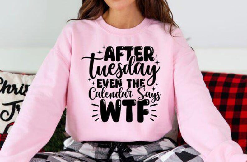 May include: A light pink sweatshirt with long sleeves. The front of the sweatshirt features the black text "AFTER Tuesday EVEN THE Calendar Says WTF". The sweatshirt is part of a clothing collection.