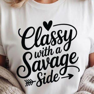 May include: White t-shirt with the phrase "Classy with a Savage Side" in black script. The design includes a heart, arrow, and the words in a stylish font. The shirt is worn with a beige sweater.