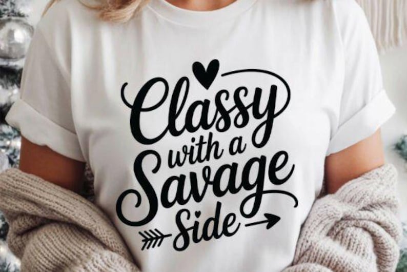 May include: White t-shirt with the phrase "Classy with a Savage Side" in black script. The design includes a heart, arrow, and the words in a stylish font. The shirt is worn with a beige sweater.