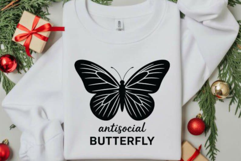 May include: White sweatshirt featuring a large black butterfly design with the words "antisocial BUTTERFLY" in a bold font. The design is centered on the front of the shirt. The sweatshirt is surrounded by holiday decorations.