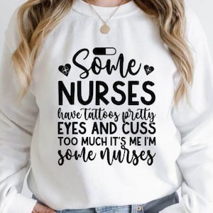 May include: A white sweatshirt featuring the black text: "Some Nurses have tattoos pretty eyes and cuss too much it's me I'm some nurses". The design includes a pill and heart symbols. The sweatshirt is a casual style.