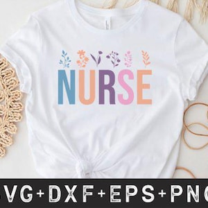May include: White t-shirt with the word "NURSE" in colourful block letters. Floral designs in pastel colours are above the word. The shirt is on a white surface with a woven placemat and decorative elements.