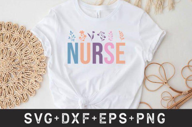 May include: White t-shirt with the word "NURSE" in colourful block letters. Floral designs in pastel colours are above the word. The shirt is on a white surface with a woven placemat and decorative elements.
