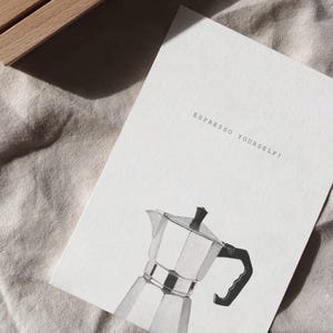 Puede incluir: Una tarjeta blanca con el texto "Espresso Yourself!" impreso en negro. Debajo del texto hay una ilustraci&oacute;n en blanco y negro de una cafetera moka.