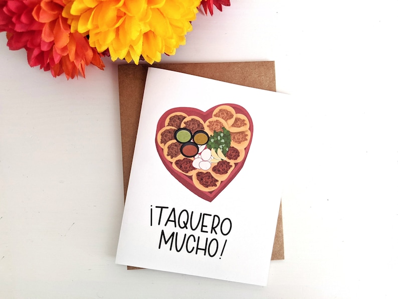 May include: A white card with a brown envelope. The card has a heart-shaped illustration of a taco platter with various toppings. The text on the card reads "&iexcl;Taquero Mucho!"