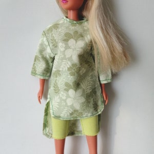 May include: A doll wearing a green floral print tunic with a yellow pair of shorts.