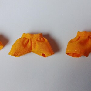 May include: Three pairs of yellow fabric doll shorts of different sizes.