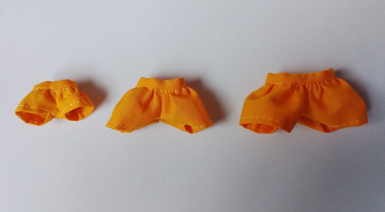 May include: Three pairs of yellow fabric doll shorts of different sizes.