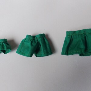 May include: Three green fabric shorts of different sizes. The shorts are made of a soft, smooth fabric and have a simple design.