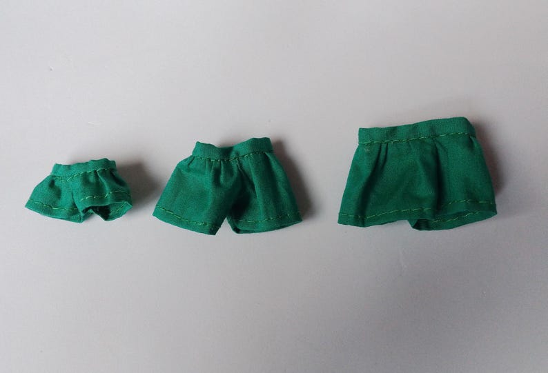 May include: Three green fabric shorts of different sizes. The shorts are made of a soft, smooth fabric and have a simple design.