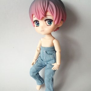 Könnte beinhalten: Eine kleine Puppe mit rosa und grauem Haar, die eine blaue Jeans trägt.