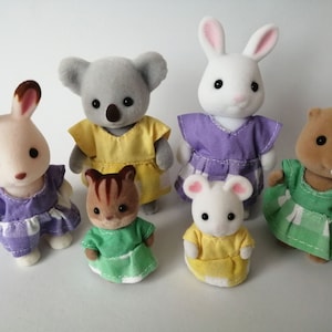Puede incluir: Un conjunto de seis figuritas de animales de peluche vestidas con vestidos coloridos. Las figuritas incluyen un koala, un conejo, una ardilla, un ratón, un castor y otro conejo.
