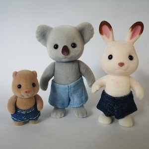 Peut inclure: Trois animaux en peluche portant des shorts en jean. Un koala gris, un castor brun et un lapin blanc.