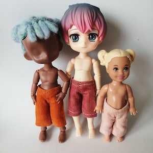 May include: Three dolls with different hairstyles and clothing. The doll on the left has blue hair and is wearing orange pants. The doll in the middle has pink hair and is wearing red pants. The doll on the right has blonde hair and is wearing pink pants.