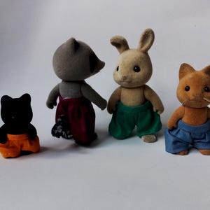 May include: Four plush toy animals wearing pants. A black cat wearing orange pants, a raccoon wearing burgundy pants, a brown rabbit wearing green pants, and an orange cat wearing blue pants.