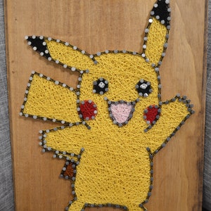 May include: A string art piece depicting Pikachu, a popular Pokemon character, on a wooden background. The character is made of yellow string wrapped around nails, with black and red string accents for the eyes and cheeks.
