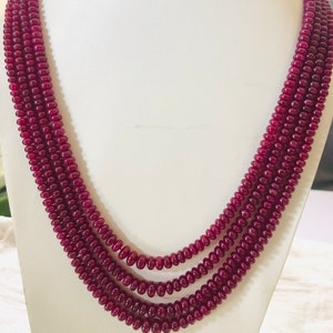 Może przedstawiać: Wielorzędowy naszyjnik wykonany z ciemnoczerwonych koralików z kamieni szlachetnych. Naszyjnik składa się z czterech rzędów koralików, każdy rząd ma średnicę około 1,2 cm. Koraliki są okrągłe i gładkie.