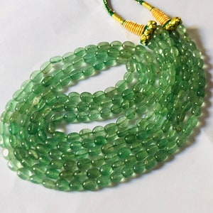 May include: A necklace composed of multiple strands of light green, oval-shaped beads. The beads are strung together and tied with a gold and green cord. The necklace is displayed on a white surface.