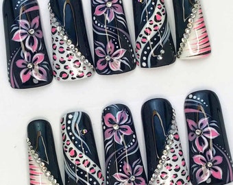May include: Set of ten black press-on nails with pink and white floral designs and rhinestones.