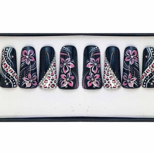 Puede incluir: Un conjunto de diez u&ntilde;as postizas negras con dise&ntilde;os florales rosas y blancos y pedrer&iacute;a.