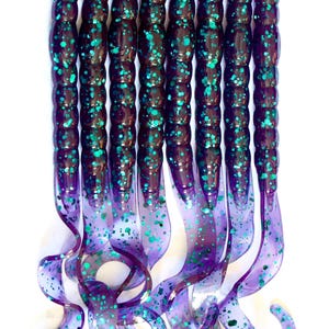 May include: A collection of purple and teal fishing lures. The lures have a segmented body with teal glitter and a curly tail. The lures are arranged vertically against a white background.