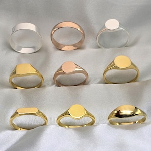 Peut inclure: Collection de neuf bagues de différents modèles et finitions. Les bagues comprennent une bague argentée, une bague en or rose et plusieurs chevalières avec des faces rondes, carrées et rectangulaires. Les bagues sont présentées sur une surface blanche texturée.