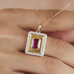 May include: A gold pendant necklace featuring a rectangular center with a deep pink gemstone. The pendant is framed by a border of small white stones and hangs from a delicate gold chain. The design is geometric with a polished gold finish.