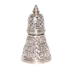 May include: A silver sugar shaker with an intricate floral design. The shaker has a domed lid with a small finial on top.