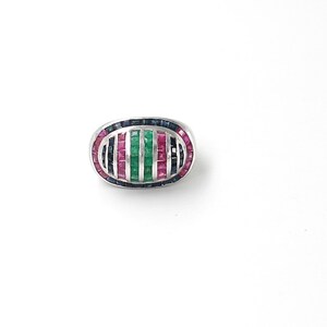 Puede incluir: Un anillo ovalado con una banda plateada. El anillo está adornado con un patrón de rayas verticales alternas de piedras preciosas rojas, verdes y azules. Las piedras preciosas son rectangulares y están muy juntas.