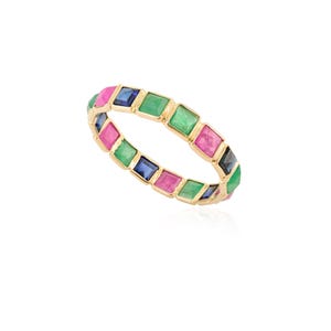 May include: A gold ring featuring a repeating pattern of colorful square gemstones. The gemstones are in shades of pink, green, blue, and black. The ring is set against a white background.