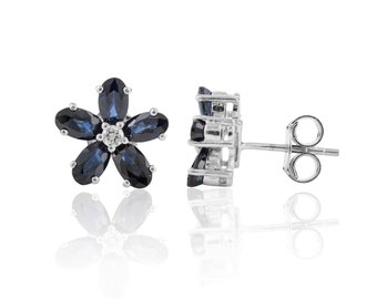 Puede incluir: Un par de pendientes de botón de plata en forma de flor con piedras de zafiro azul y un solo diamante en el centro de cada flor.