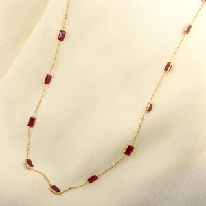 May include: A gold chain necklace with rectangular red gemstones. The necklace is on a white background.