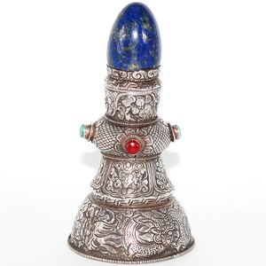May include: A silver bell with intricate carvings and a lapis lazuli egg on top. The bell is decorated with turquoise and red gemstones.