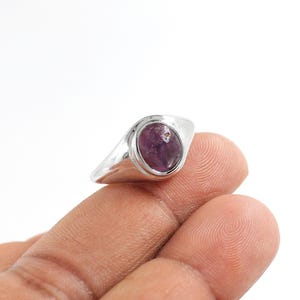 Op de afbeelding: Een zilveren ring met een paarse ovale edelsteen in het midden.