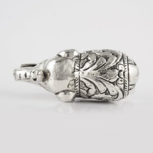 May include: A silver elephant figurine with intricate floral designs. The elephant is lying on its side with its trunk raised.