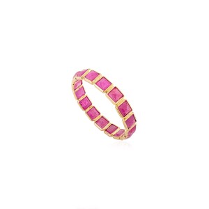 Könnte beinhalten: Ein goldener Ring mit einem durchgehenden Band aus quadratischen, leuchtend rosa Edelsteinen. Die Edelsteine sind eng aneinander gesetzt und bilden ein volles, auffälliges Design. Der Ring ist vor einem weißen Hintergrund platziert.