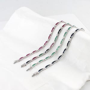 Pode incluir: Quatro pulseiras de prata com pedras preciosas coloridas alternadas: rubi, esmeralda, safira e ônix. Cada pulseira apresenta pedras retangulares engastadas numa corrente de prata, com pequenas pedras transparentes.