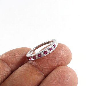 Könnte beinhalten: Ein Silberring mit einer Reihe quadratischer roter Rubine und kleineren weißen Diamanten, die in die Band gefasst sind.