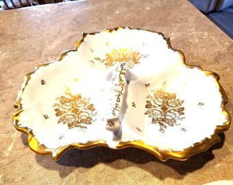 May include: A white, three-sectioned serving dish with a gold scalloped edge. The dish features gold floral designs and a gold handle. The interior is white, and the exterior edge is gold.