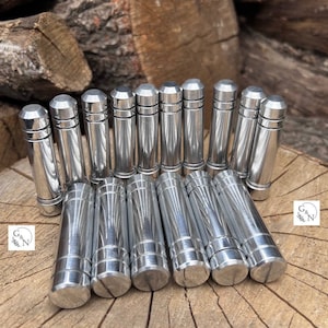 Puede incluir: Un grupo de 14 tubos de metal plateado con un diseño acanalado. Los tubos están dispuestos en una fila sobre una superficie de madera.