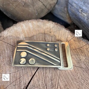May include: A brass belt buckle with a geometric design featuring a series of lines and circles.