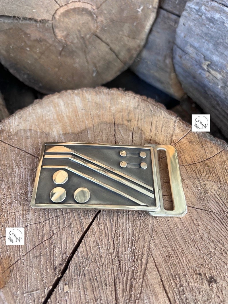 May include: A brass belt buckle with a geometric design featuring a series of lines and circles.