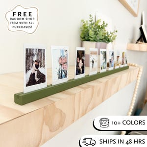 Może przedstawiać: Zielona drewniana półka na zdjęcia z kilkoma małymi zdjęciami. Półka znajduje się na jasnej drewnianej powierzchni. Widoczny jest tekst "10+ KOLORÓW".