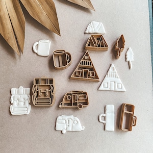 May include: A set of 11 brown and white cookie cutters shaped like camping and outdoor-themed items, including a tent, a camper, a mug, a backpack, and a tree.