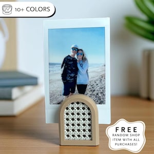May include: A photo holder with a beige frame and a woven cane design, holding a photo of a couple at the beach. The photo holder is on a wooden surface. The image also includes text that says "10+ COLORS".