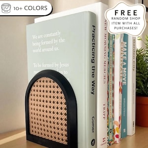 May include: A black and natural woven cane bookend holds a row of books. The bookend has an arched design and a rectangular base. The books have titles such as "Practicing the Way" and "Make a Move".