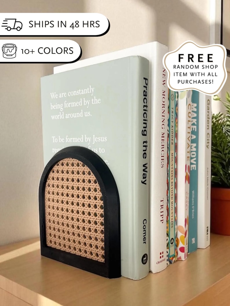 May include: A black and natural woven cane bookend holds a row of books. The bookend has an arched design and a rectangular base. The books have titles such as "Practicing the Way" and "Make a Move".