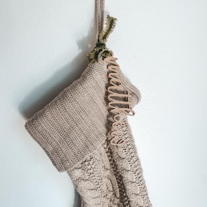 May include: A beige knitted stocking with a wooden tag that says "little ones" hanging from it.