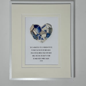 Könnte beinhalten: Ein gerahmtes Wandbild mit einer Herzform, die aus verschiedenen blauen und weißen Keramikscherben zusammengesetzt ist. Unter dem Herz steht der Text: She is a beautiful piece of broken pottery, put back together by her own hands.