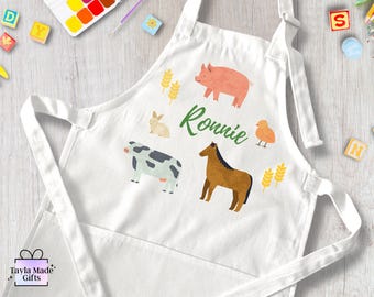 May include: White apron with a pocket, featuring a farm animal theme. The apron has a brown horse, a pink pig, a black and white cow, a white rabbit, and a yellow chick. The name "Ronnie" is written in green cursive on the apron.